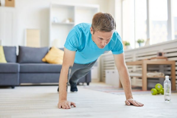 a man in a blue shirt doing pushups from home in his living room
