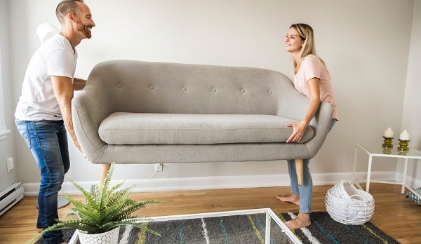 A couple lifting up a couch in the living room